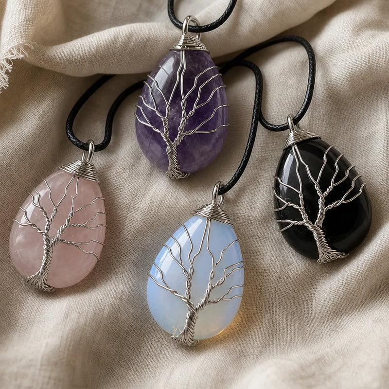 Four teardrop-shaped crystal pendants with silver tree-of-life wirework, shown on black cords against a beige linen fabric background. The stones are rose quartz, amethyst, opalite and 