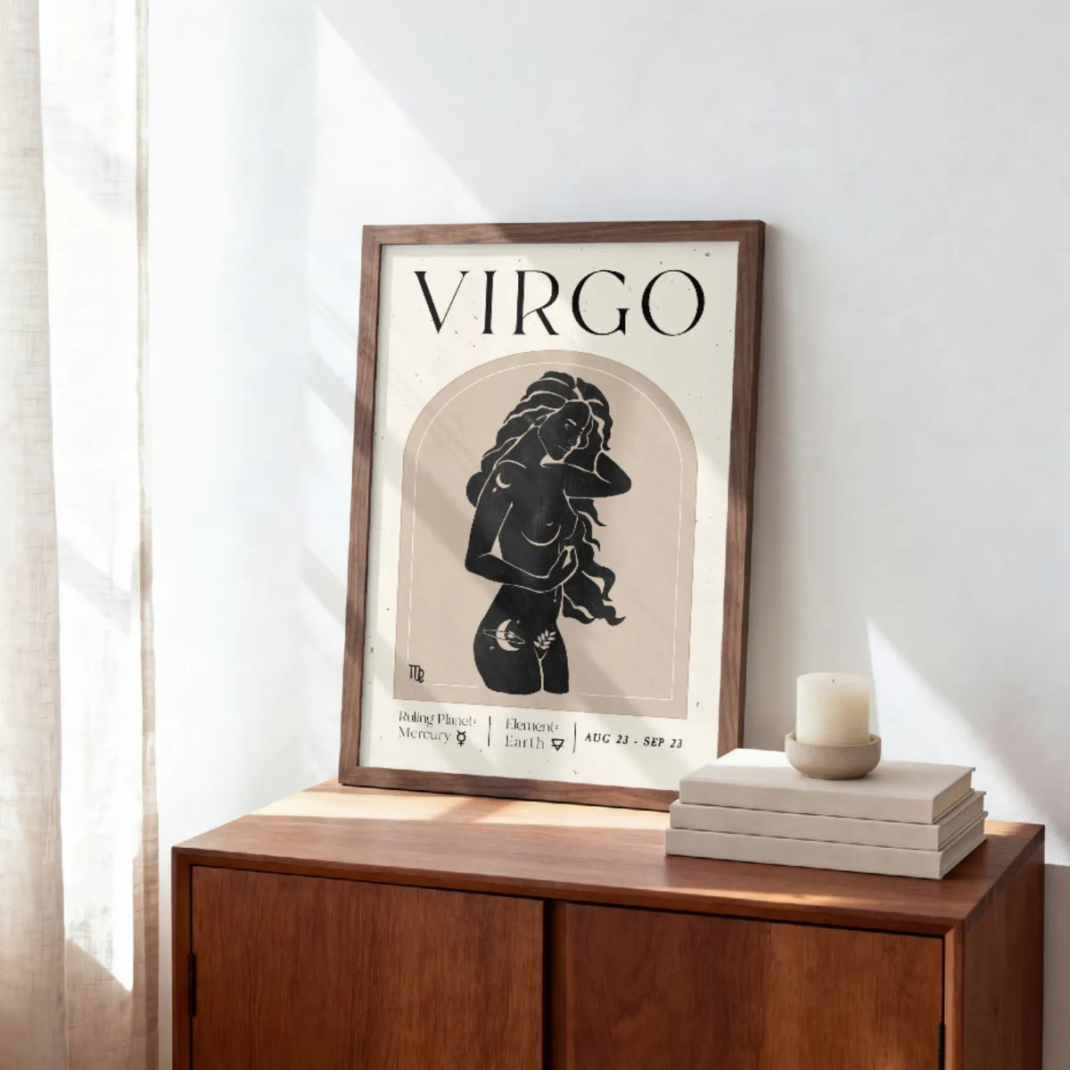 A framed art print featuring a black and beige illustration of a Virgo woman with the word 'VIRGO' at the top, leaning on a wooden cabinet next to a candle and books in a bright room.